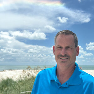 Mike Hetrick on the beach in FL with teal Clarus shirt on